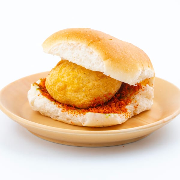 A vada pav, an Indian street food, on a light brown plate against a white background.