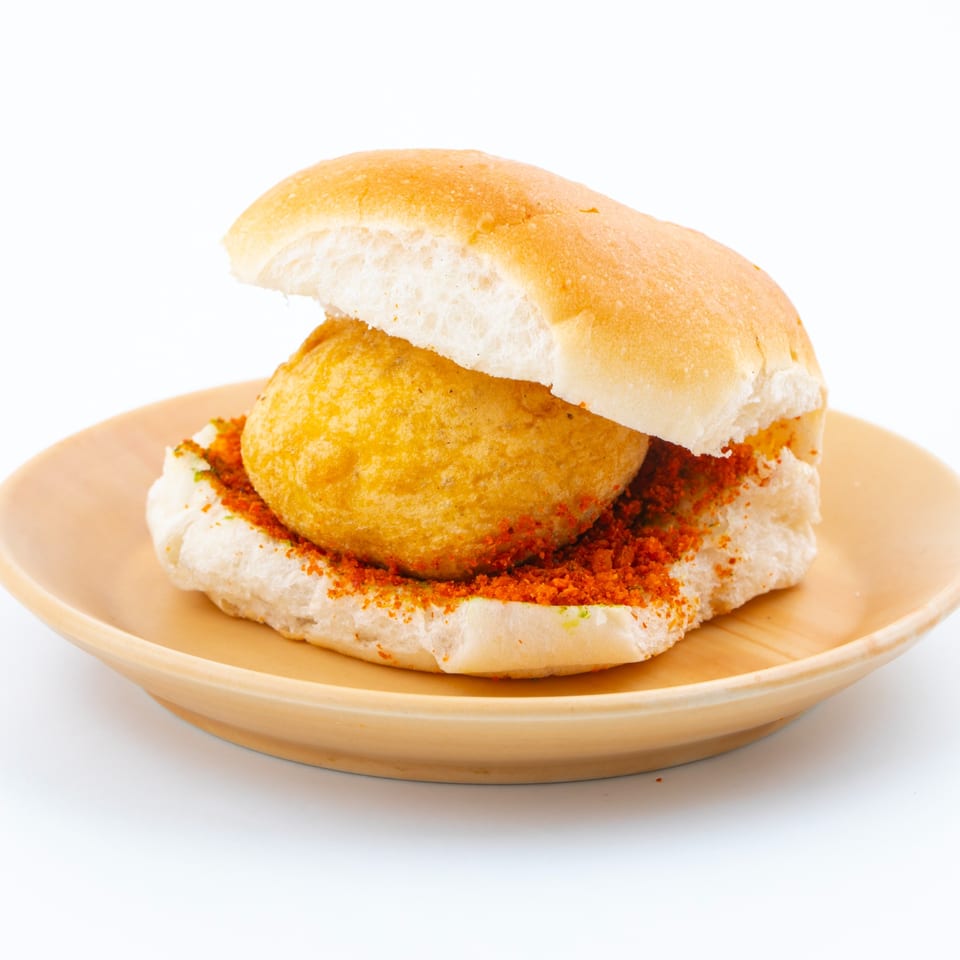 A vada pav, an Indian street food, on a light brown plate against a white background.