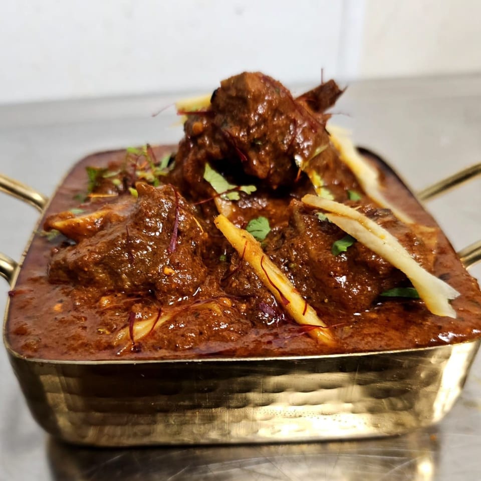 Rich Indian lamb curry, garnished with ginger and cilantro, served in a golden bowl.