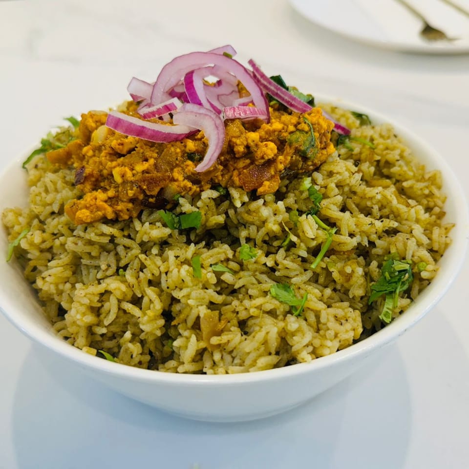 A bowl of Indian green rice topped with yellow curry and sliced red onions.