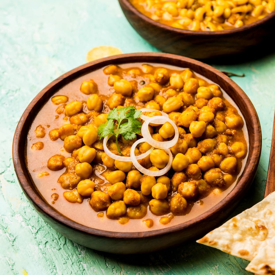 Chana Masala, an Indian chickpea curry, garnished with cilantro and onion in a wooden bowl.