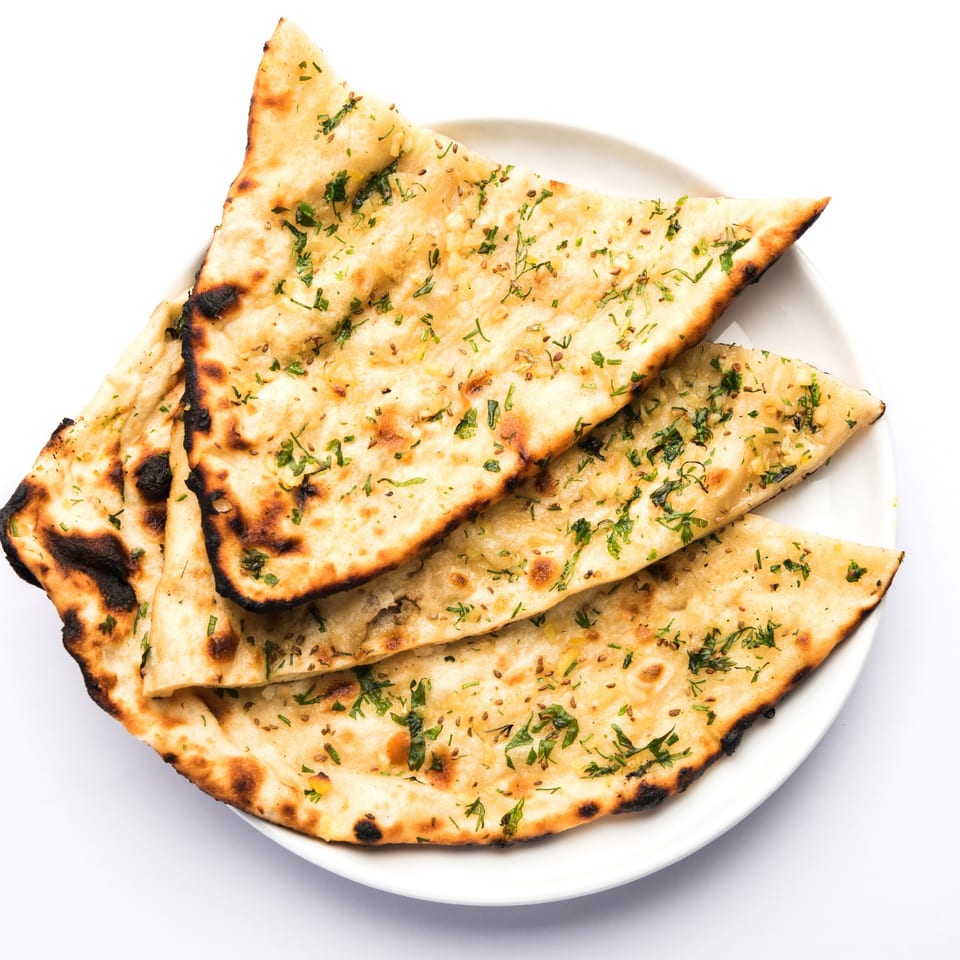 Three pieces of golden-brown Indian naan bread, garnished with herbs and spices, on a white plate.