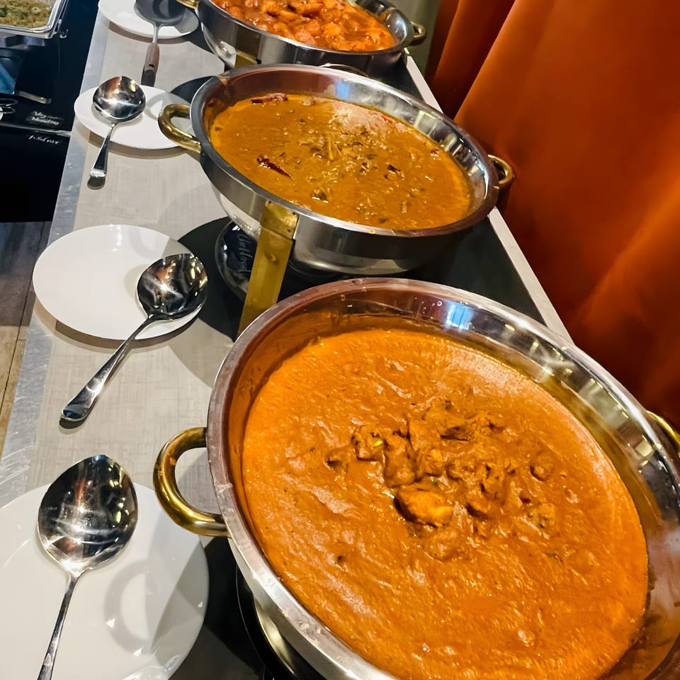 Three large silver chafing dishes filled with different Indian curries on a buffet line.